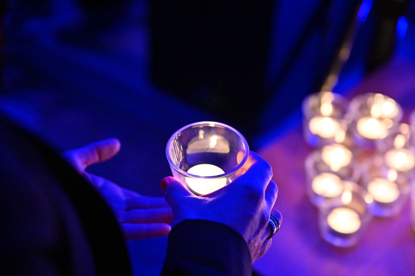 Eine Hand hält ein Teelicht im Glas, dahinter weitere Kerzen