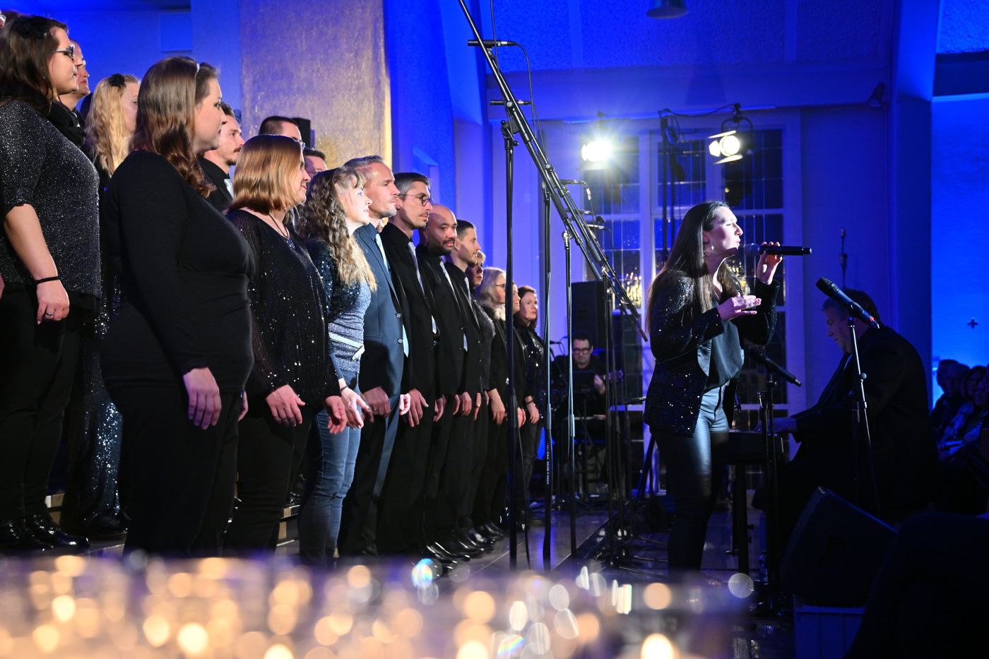 Eine Solistin singt vor dem Chor, im Vordergrund leuchten Kerzen